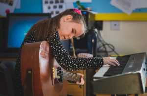 A young girl passionately learning to use piano and guitar